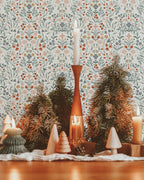 Holiday scene with wooden trees, candles, and greenery styled in front of a vintage-inspired floral wallpaper from Riverpine.