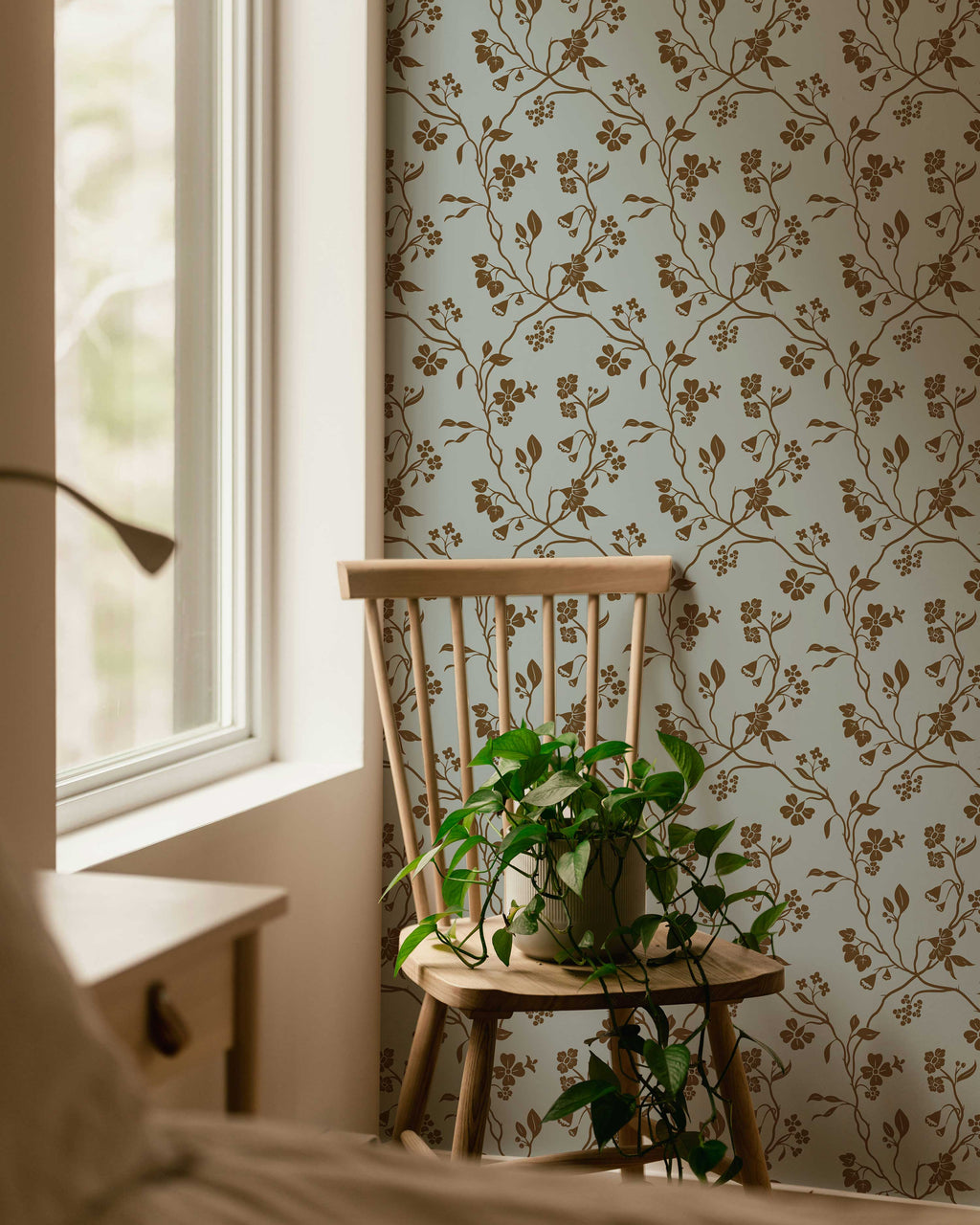 Floral wallpaper with a wooden chair and plant in a room with natural light.