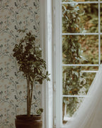 Potted plant next to a window with floral wallpaper