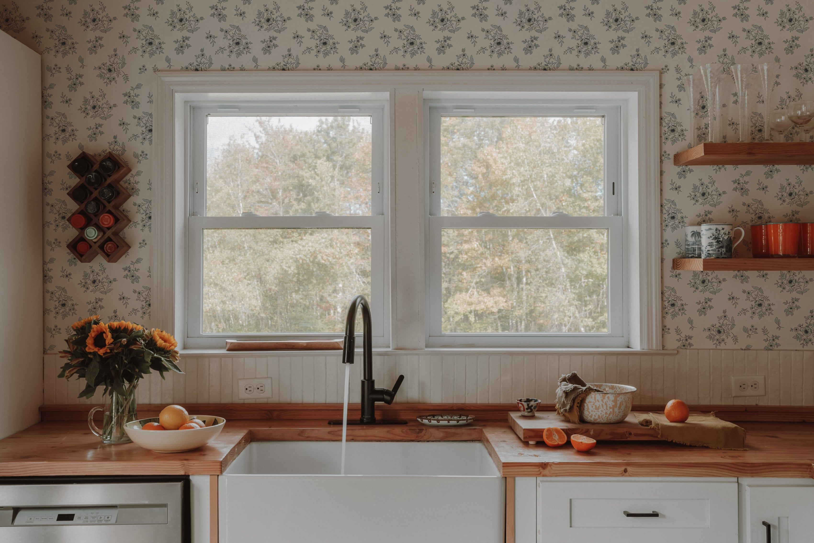 Kitchen with a large window, wooden countertops, and floral wallpaper.