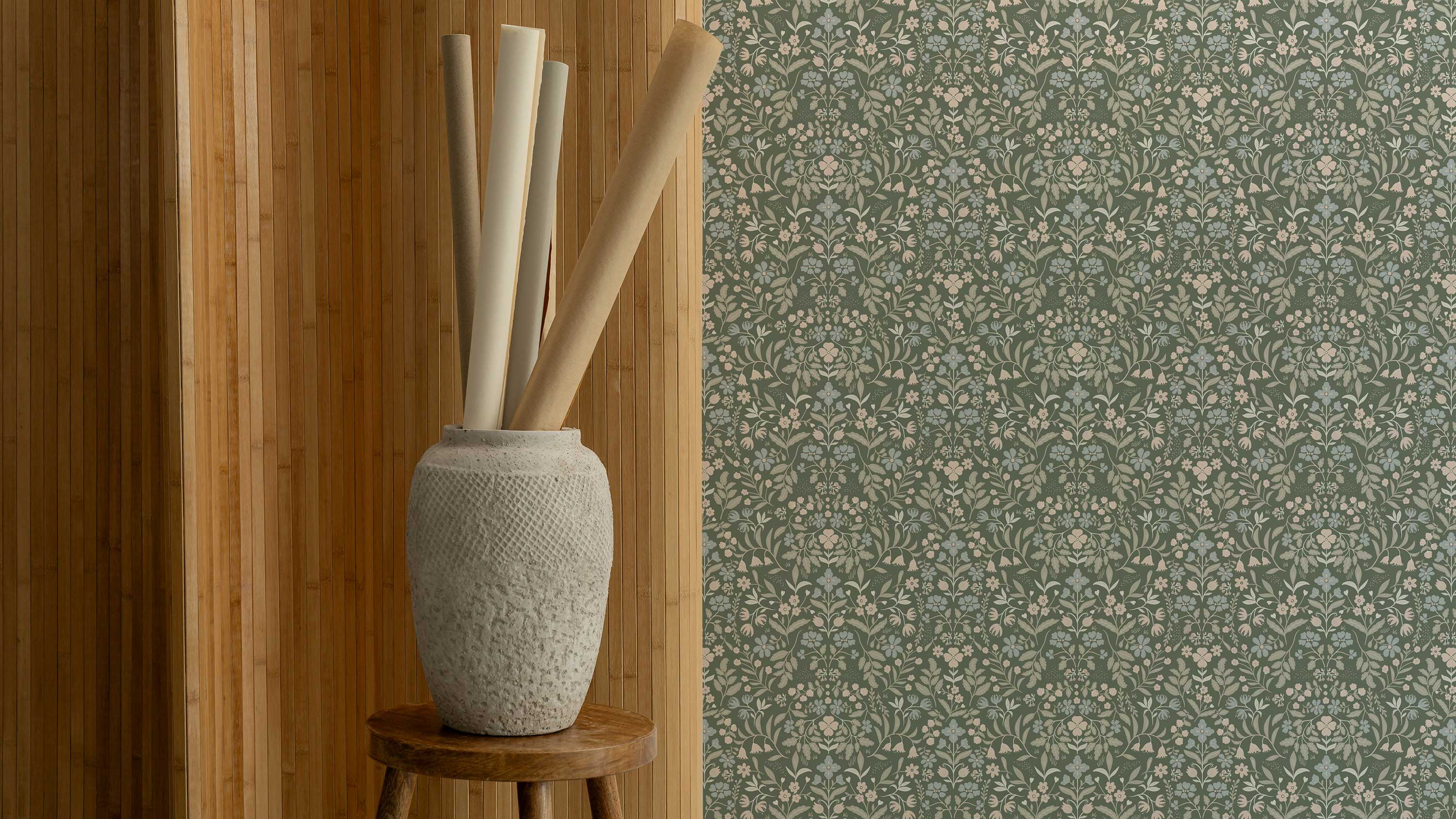 Decorative vase with sticks on a wooden stool against a floral wallpapered wall.