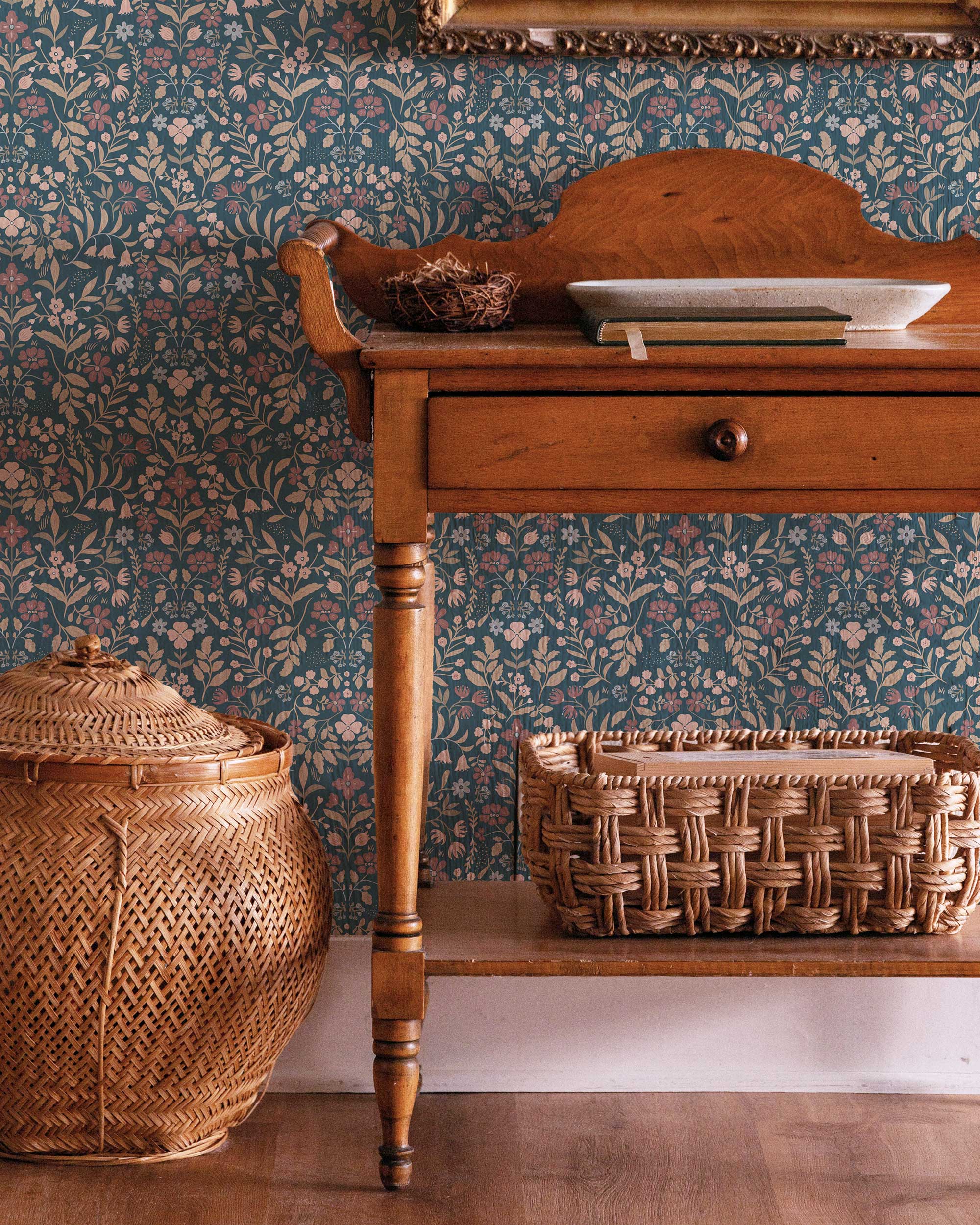 Wooden side table with wicker basket and decorative items against a patterned wallpaper.