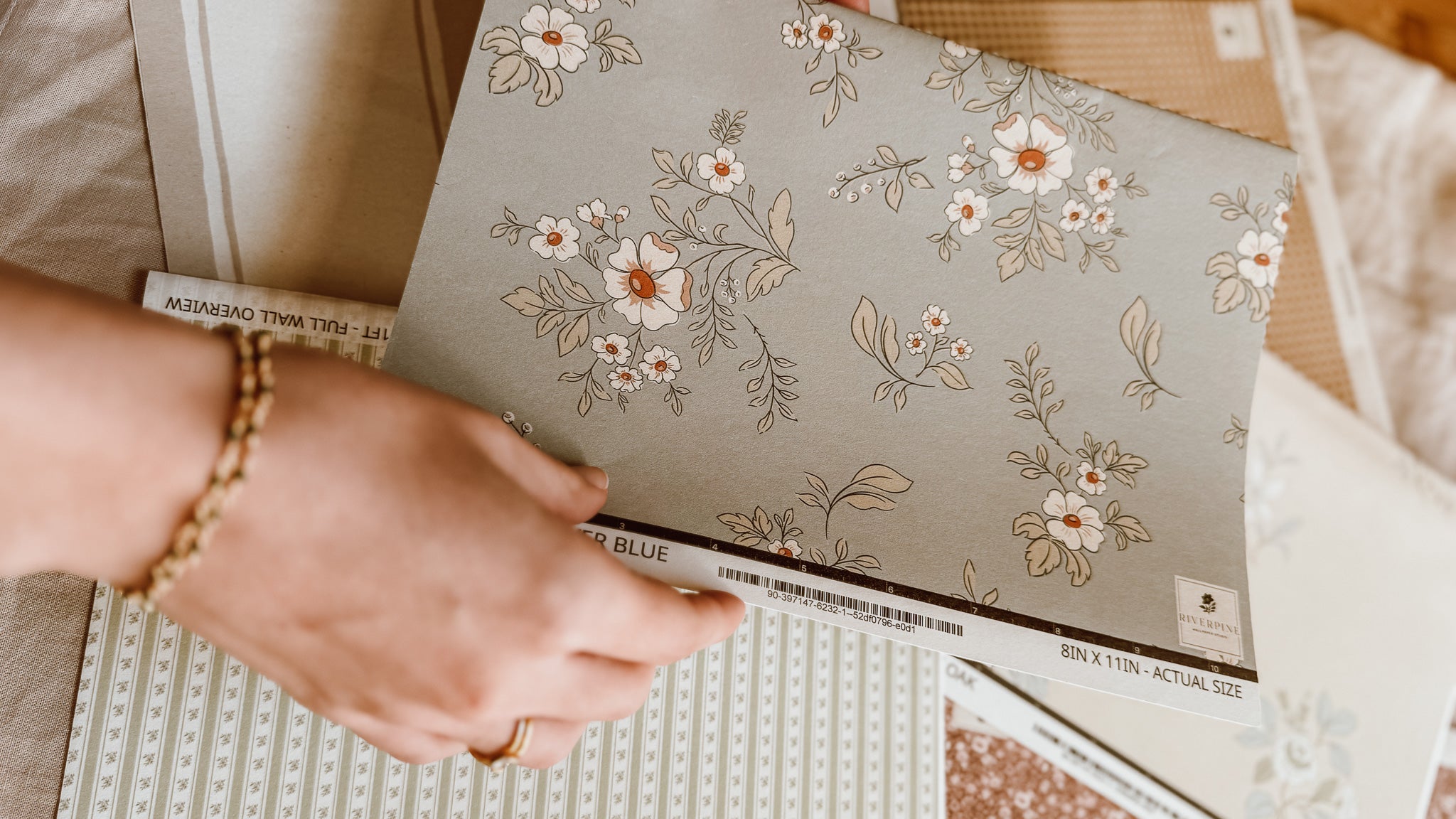 Person holding a floral-patterned wallpaper sample