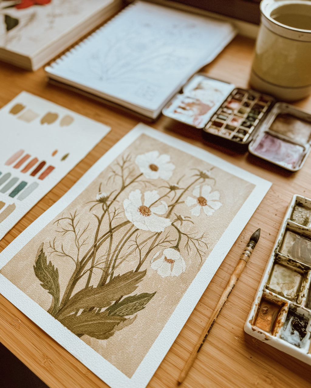 Artistic floral design on a textured surface with watercolor supplies.