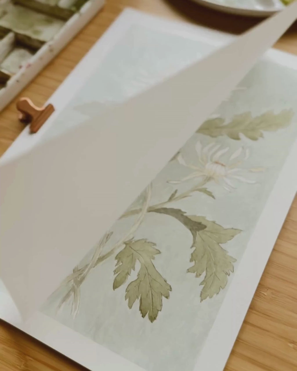 Video showing Danelys Sidron gently lifting the cover sheet to reveal the hand-painted Chrysanthemum watercolor print for The Conservatory Print Club November edition.