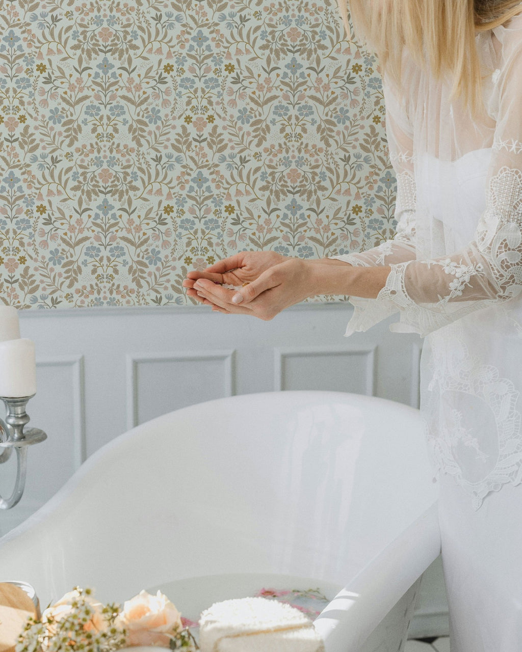 Woman in a white dress sitting in a room with floral wallpaper.