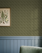 Wild Geranium wallpaper in earthy olive with floral motifs in a vintage living room setting.